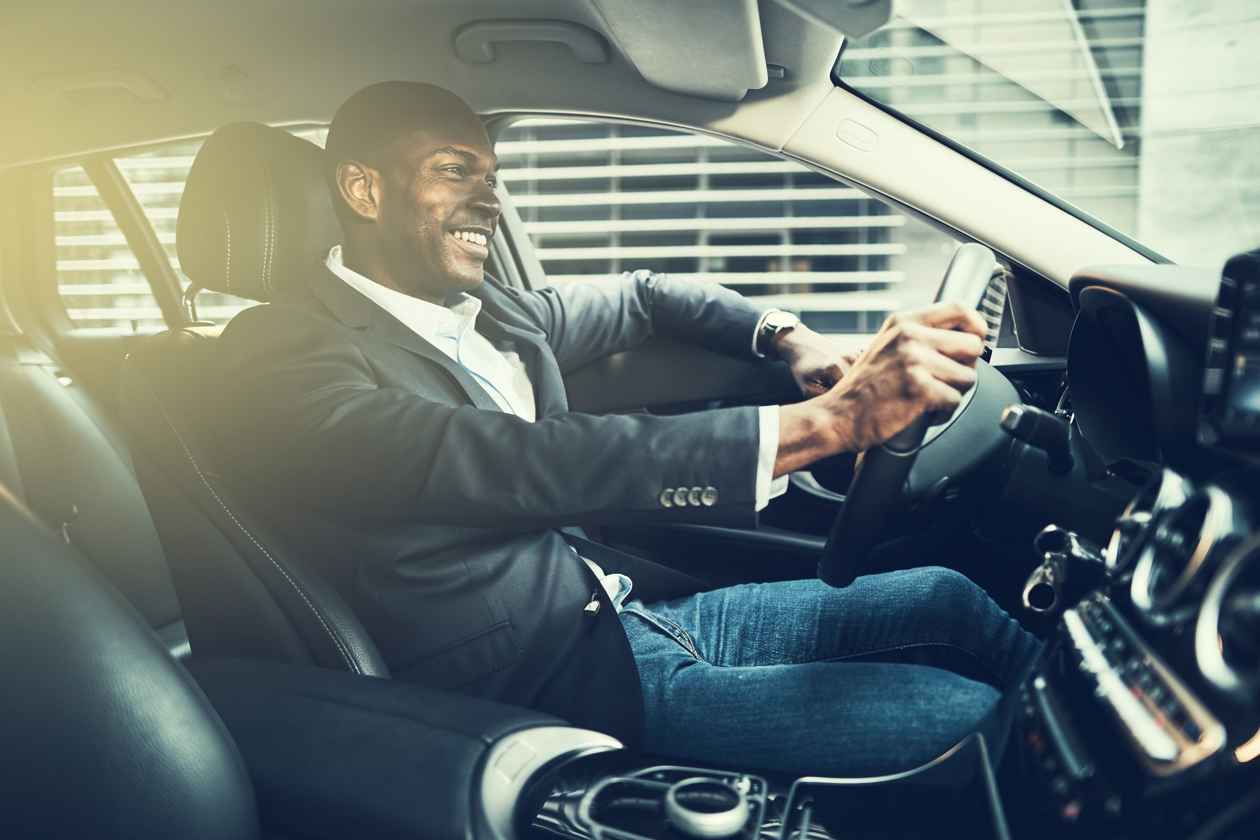 African businessman wearing a blazer and smiling while driving his car during his morning commute through the city